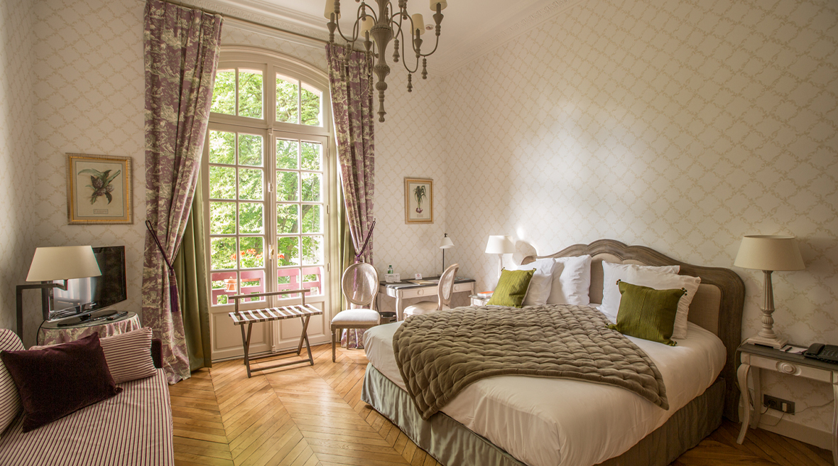 A luxurious guest room with double bed, chandelier and large french windows leading out on to the balcony
